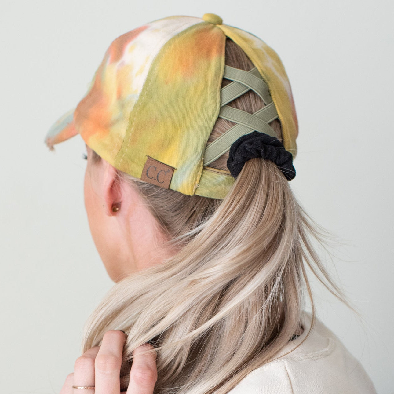 Person wearing a tie-dye cap with a scrunchie in their hair against a plain background
