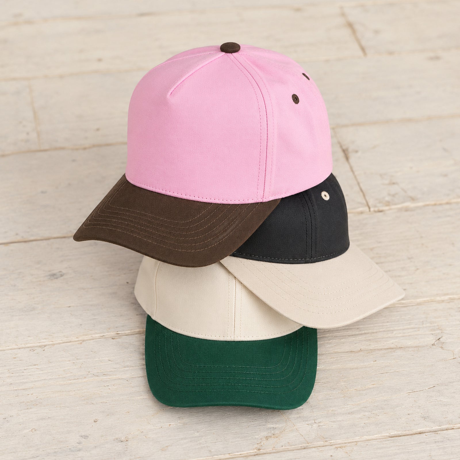 TCM0002 canvas caps stacked on pale wood in Brown/Pink, Cream/Black, and Dark Green.