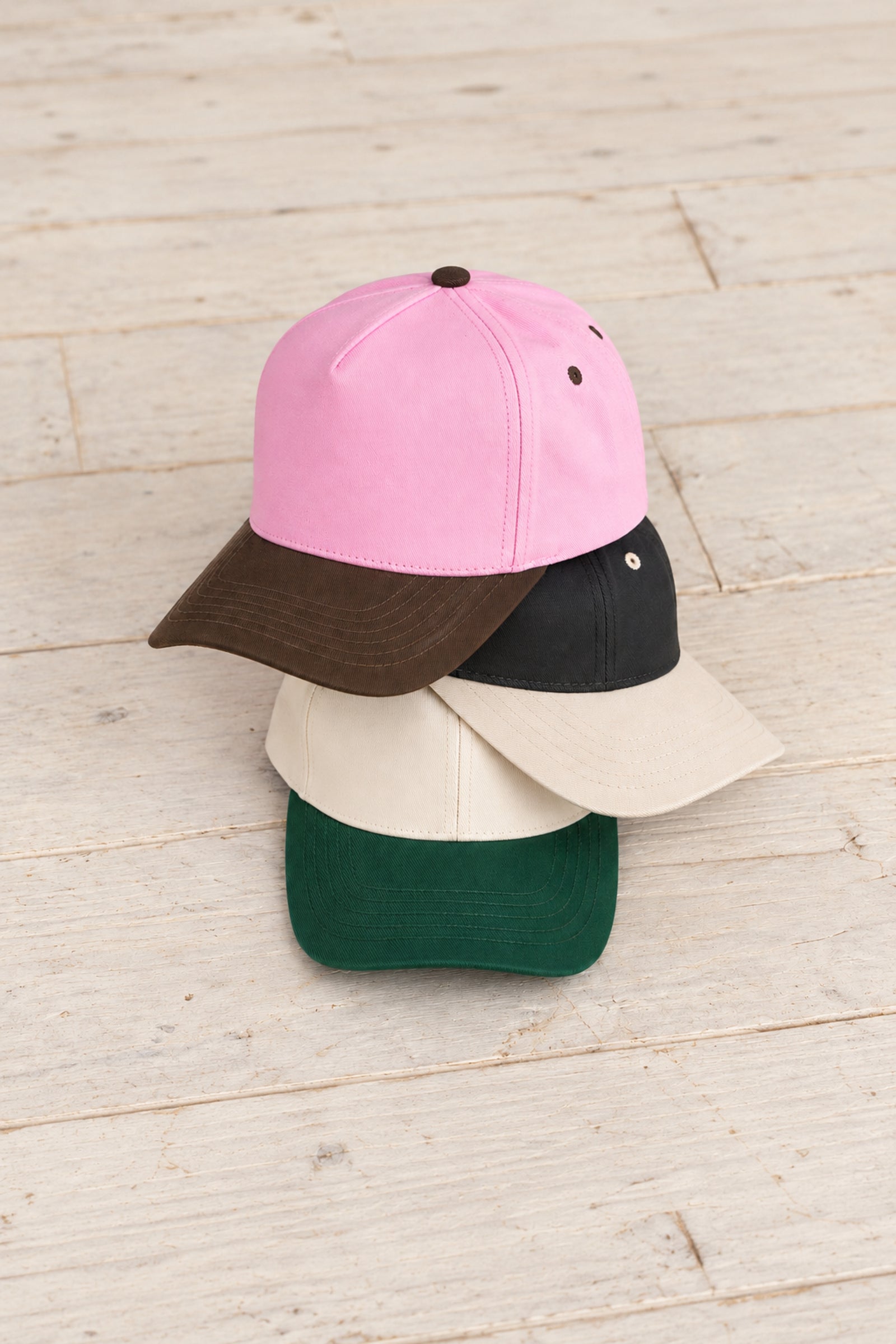 TCM0002 canvas caps stacked on pale wood in Brown/Pink, Cream/Black, and Dark Green.