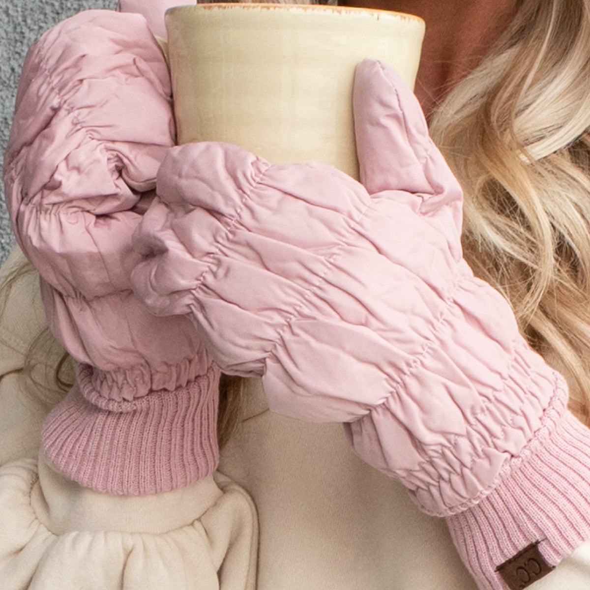 Person wearing pink gloves holding a beige mug against a neutral background