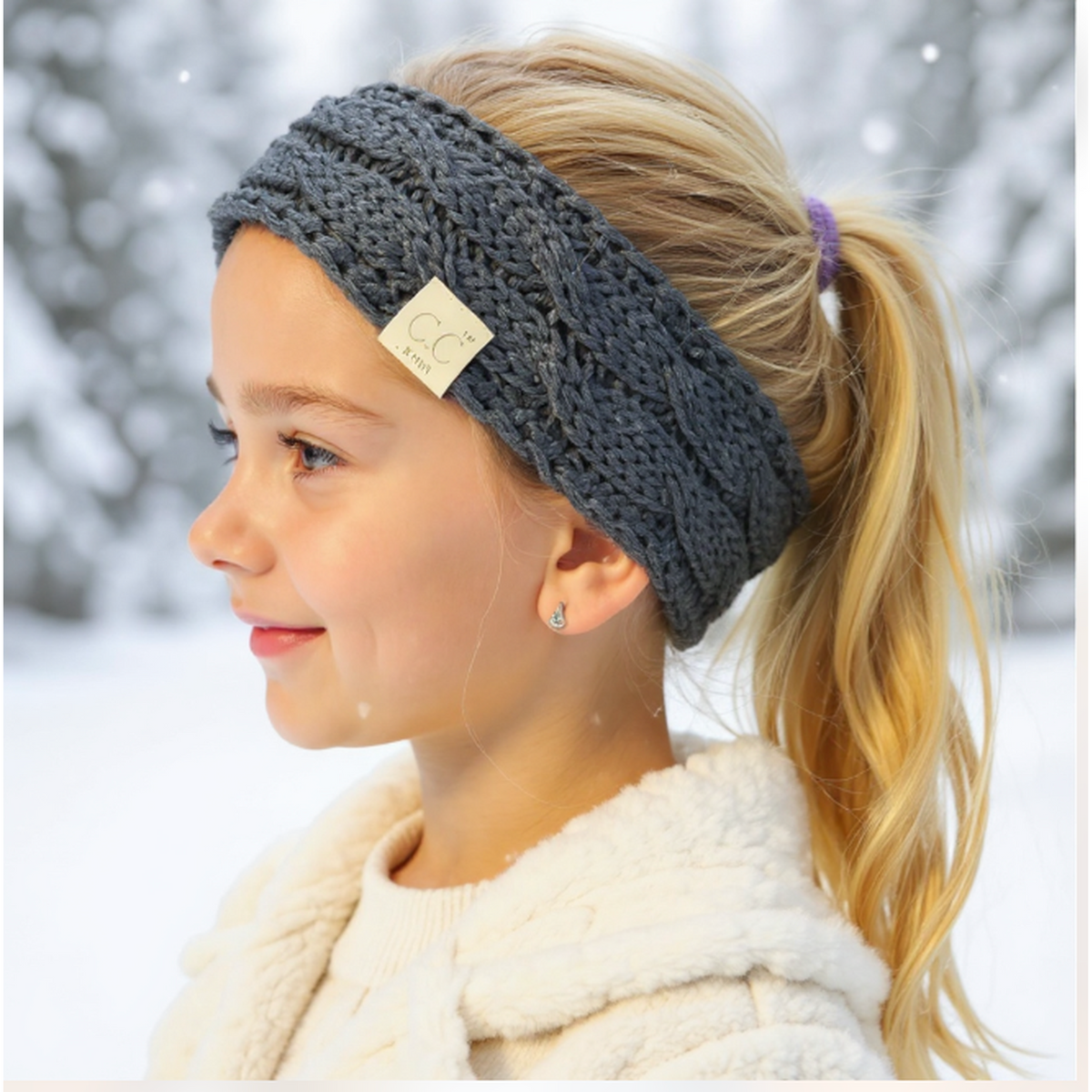 Girl wearing a gray knitted headband with a brand tag, standing in a snowy background