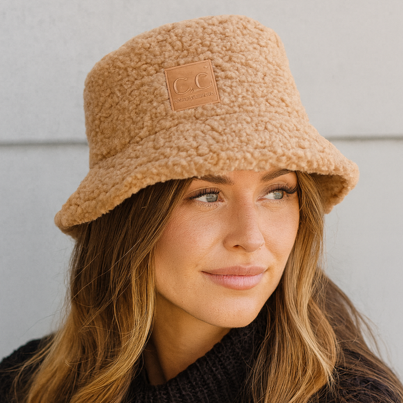 Woman wearing a tan bucket hat and black sweater against a light gray background