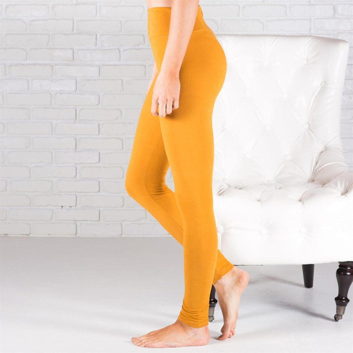 Person wearing mustard yellow leggings standing in a room with a white brick wall and white chair.