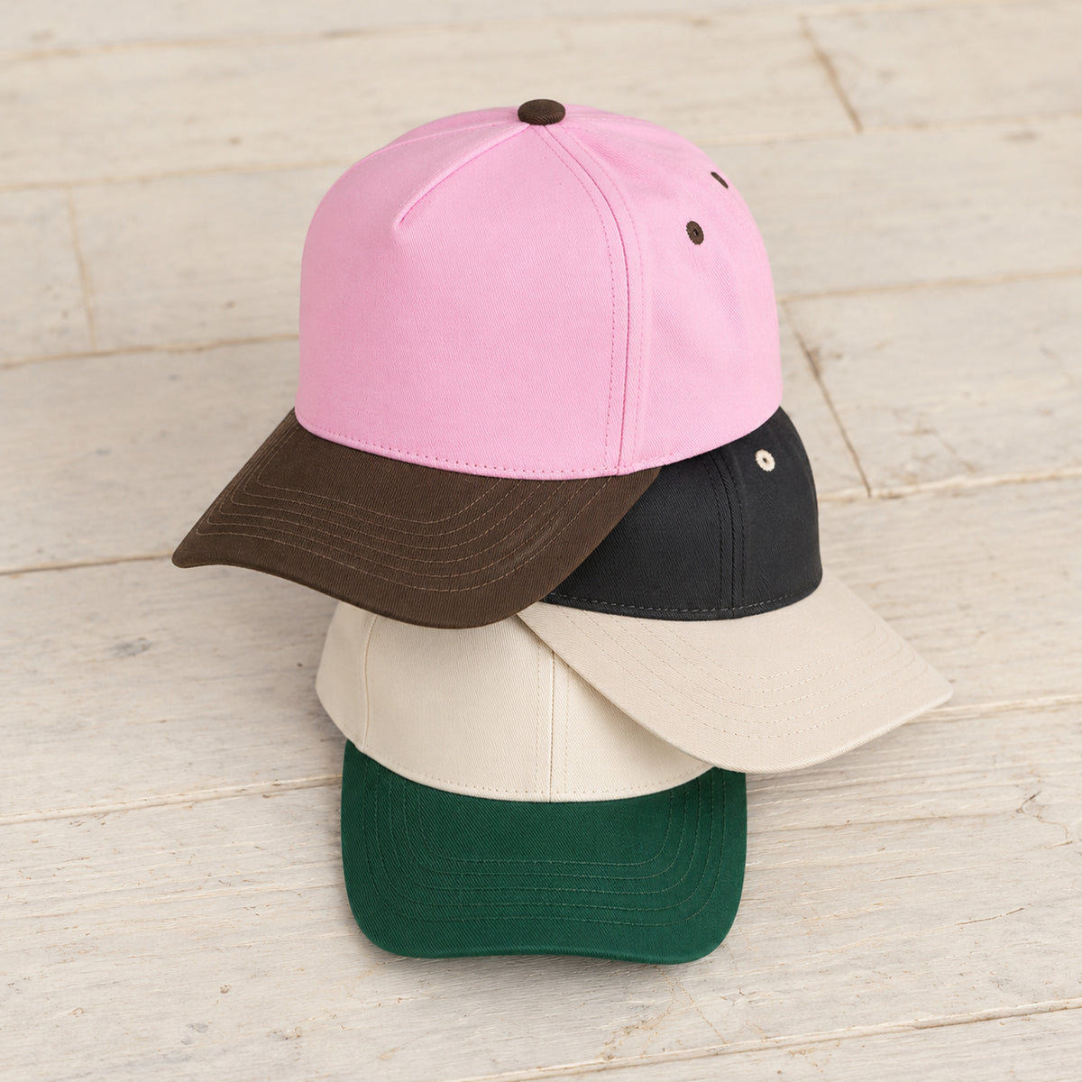 TCM0002 canvas caps stacked on pale wood in Brown/Pink, Cream/Black, and Dark Green.