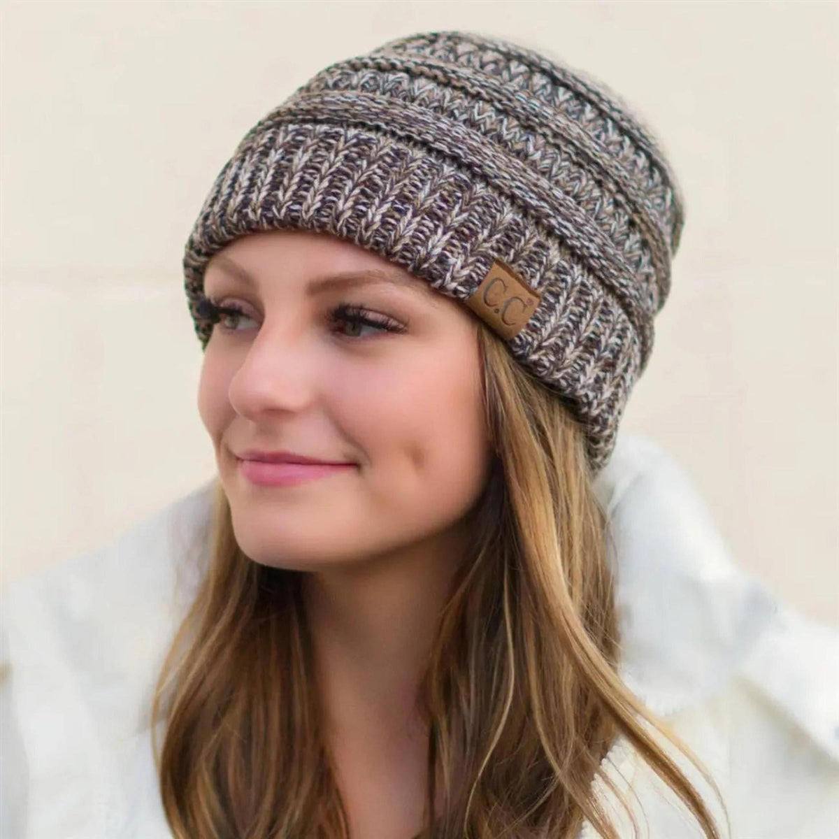Woman wearing a knitted beanie with a visible brand logo on a beige background